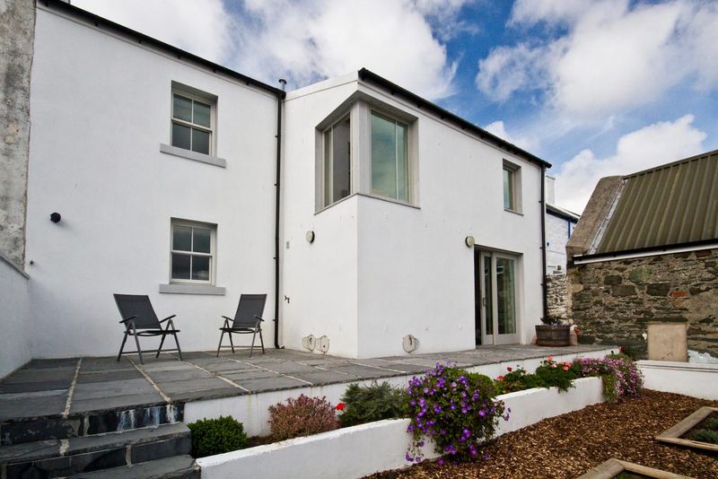 Rosgorm's enclosed garden and paved patio with two chairs, behind the whitewashed cottage