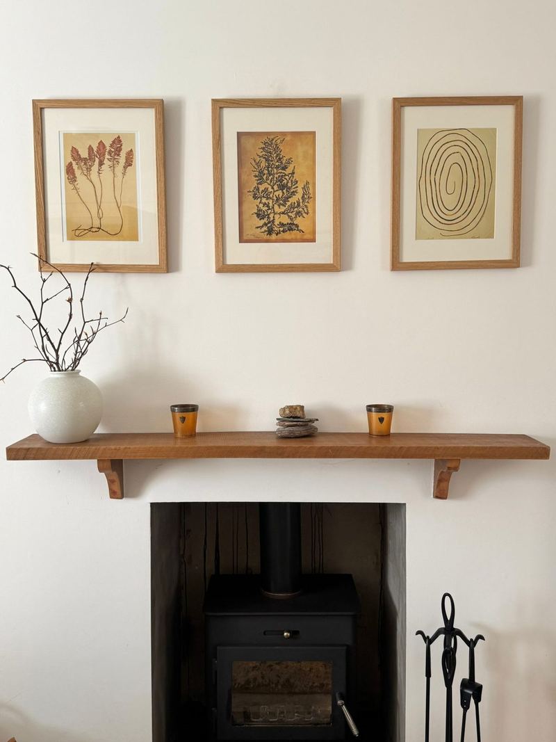 The wood-burning stove in Rosgorm's lounge, beneath a wooden mantelpiece and three framed botanical prints